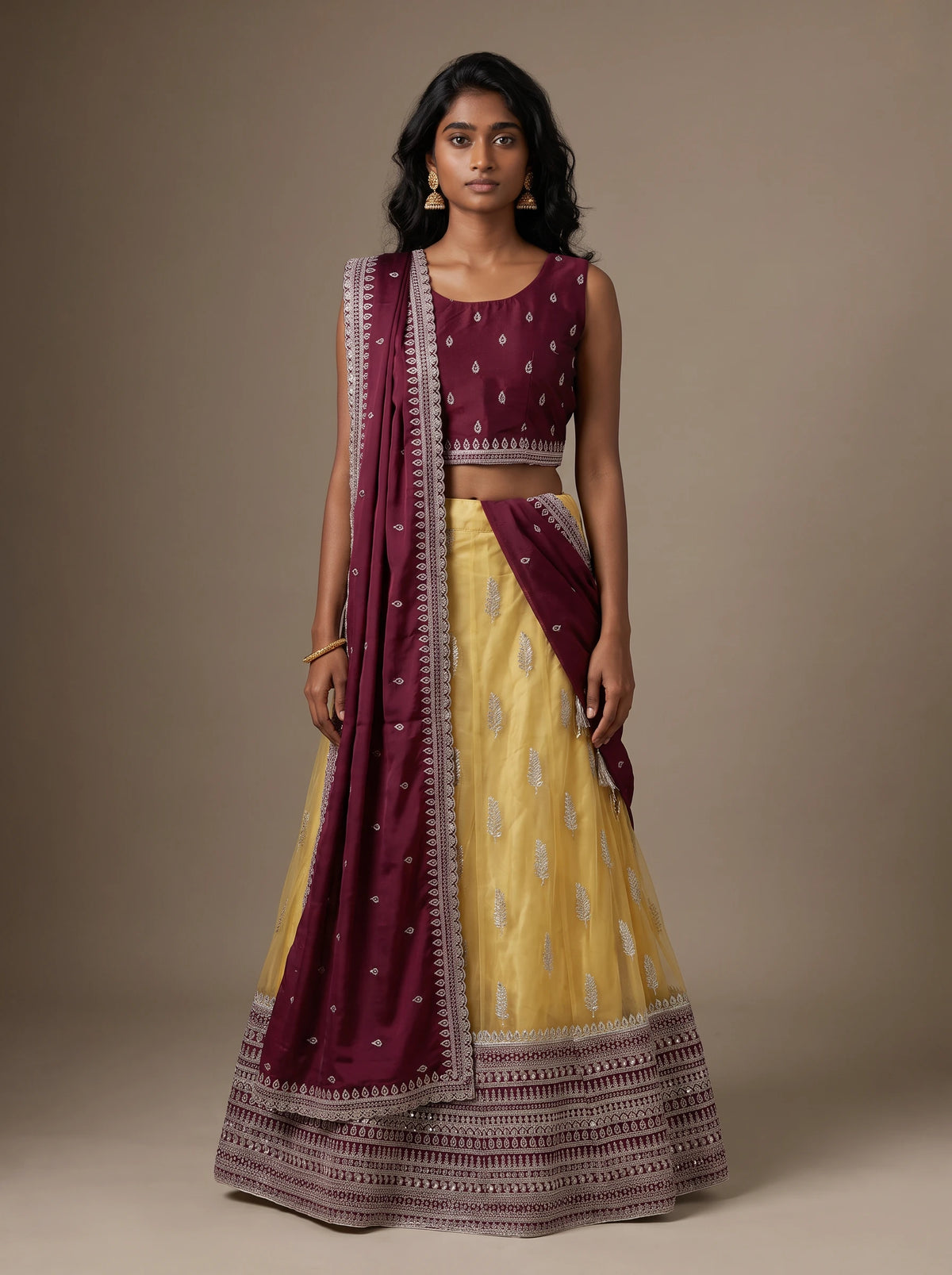Model wearing a wine and mustard yellow embroidered lehenga set with matching wine dupatta
