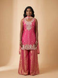 Model wearing a fuchsia pink and metallic gold tissue silk sharara set with embellished top and matching dupatta