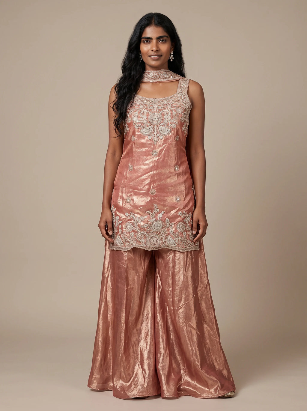 Model wearing a peach tissue silk embroidered sharara set with flared bottoms and matching dupatta.