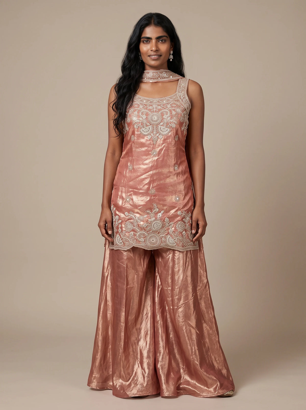 Model wearing a peach tissue silk embroidered sharara set with flared bottoms and matching dupatta.